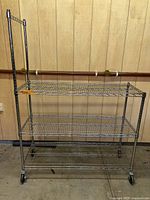 Full view of chrome wire rack showing three shelves, casters, and extended uprights with hanging bar