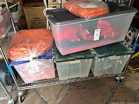 Tote bins on rolling rack containing orange waterproof clothing and other packed gear