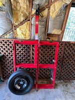 Full view of folded red trailer frame standing upright with spare tire leaning against it