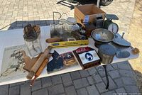 Overall view of lot items on table including signs, grinder, scale, kitchen tools and jars
