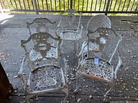 Front view of five matching white cast iron chairs with ornate openwork