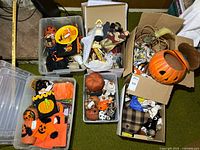 Overview of multiple boxes containing assorted Halloween decorations such as pumpkin bucket, fabric pumpkins, figurines and craft pieces