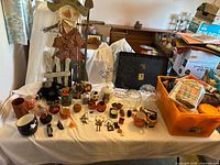 Overall view of assorted Halloween items on table including bowls, jars, figurines, scarecrow, orange tote of linens