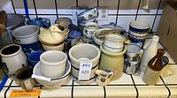 Countertop view showing assorted crocks, mugs, bowls and bottles
