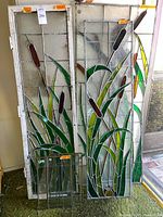 Two large stained glass panels with cattail design beside two small clear grid panes