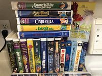 Stacked view of clamshell Disney tapes and additional titles