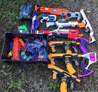 Group of Nerf blasters, pistols, bow and crate of accessories laid out on ground