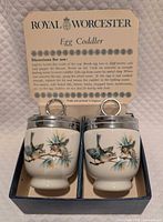 Front view of both egg coddlers in box with instruction card visible