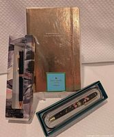 All three items together: sealed Kate Spade notebook, boxed Mitani pen, boxed black pen