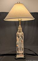 Full view of illuminated table lamp showing carved figure, shade, base