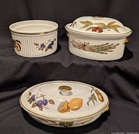 Three porcelain dishes with fruit motifs: shallow covered casserole, deep covered casserole, and soufflé dish