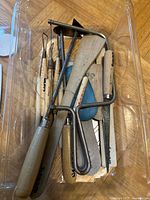 Plastic tub holding assorted pottery tools including coping saw, loop tools, ribs, file