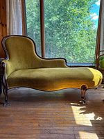 Side view of chaise lounge showing upholstery, curved frame, claw feet, light through window