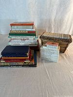 Entire lot showing two stacks of larger hardcovers, stack of Beatrix Potter books and wicker basket