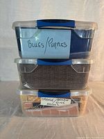 Stack of three clear plastic bins labelled Blues/Purples, middle unlabelled, bottom labelled Orange Yellow Brown