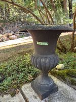 Full view of black metal urn on pedestal base outdoors