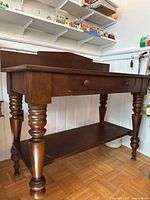 Full view of wooden buffet showing drawer, lower shelf and turned legs
