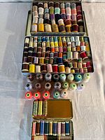Overall shot of three metal tins holding numerous thread spools and cones