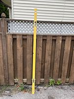 Full view of yellow 78" spirit level leaning against fence