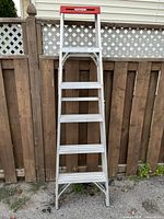 Front view of aluminum 5-step ladder leaning against fence