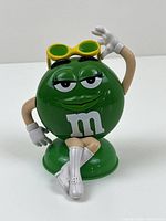 Front view of Green M&M girl figurine with sunglasses, white gloves and boots