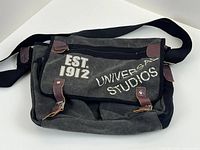 Front view of Universal Studios canvas messenger bag showing printed logo and buckle straps