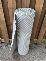 Rolled dimpled plastic membrane standing upright against wooden fence