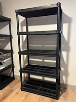 Full view of five-tier black plastic shelving unit standing against wall
