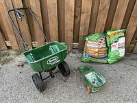 All four items: push spreader, hand spreader, sealed grass seed bag, opened fertilizer bag