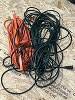 Orange and green extension cords coiled on plywood surface