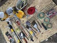 Overall lot on OSB board showing poles, pails, brushes, roller frames, tape, sanding packs