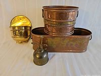 Group shot of all four items: brass mister, brass wall pocket planter, oval copper planter, cylindrical copper planter