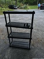 Front view of four-tier black plastic shelving unit on driveway