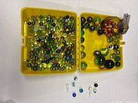 Open yellow case filled with multicolour marbles, mesh bag and loose shooters visible