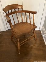Front angled view of antique pine captain's chair showing curved back, spindle supports, saddle seat and front legs