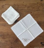 Stack and single unfolded napkin showing lace border and embroidery