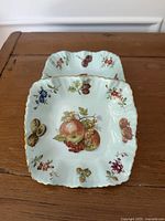 Top view of two dishes showing fruit motifs and scalloped gilt rims