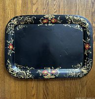 Front view of black metal tray with hand painted gold and red floral border