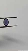 Gemstone held in tweezers showing profile and color
