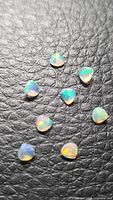 Eight small faceted teardrop opals on black textured surface
