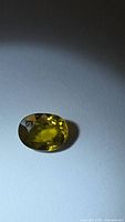 Faceted oval greenish yellow sphene under light