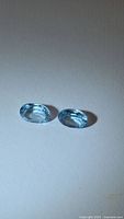 Two oval cut blue topaz gemstones on neutral background