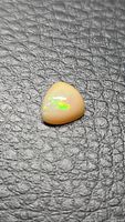 Trillion cabochon opal on textured background, showing play-of-color
