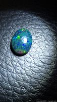 Oval cabochon opal on black surface showing multicolor flash