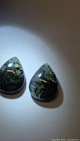Two pear cabochon prehnite stones under direct light showing color and inclusions