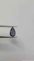 Pear cut purple spinel held in tweezers, frontal view
