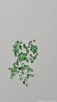 Scatter of small vivid green round-cut tsavorite garnets on neutral background
