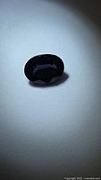 Oval faceted spinel on flat surface showing overall color
