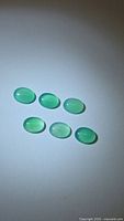 Six vivid green oval cabochon onyx gemstones arranged on light background