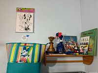 Overview of shelf with tote, print, statue, fan, framed picture, book and figurines